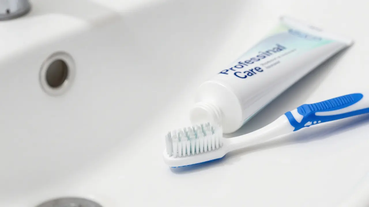 Zubní pasta s vysokým obsahem fluoridu a jemný kartáček na umyvadle.